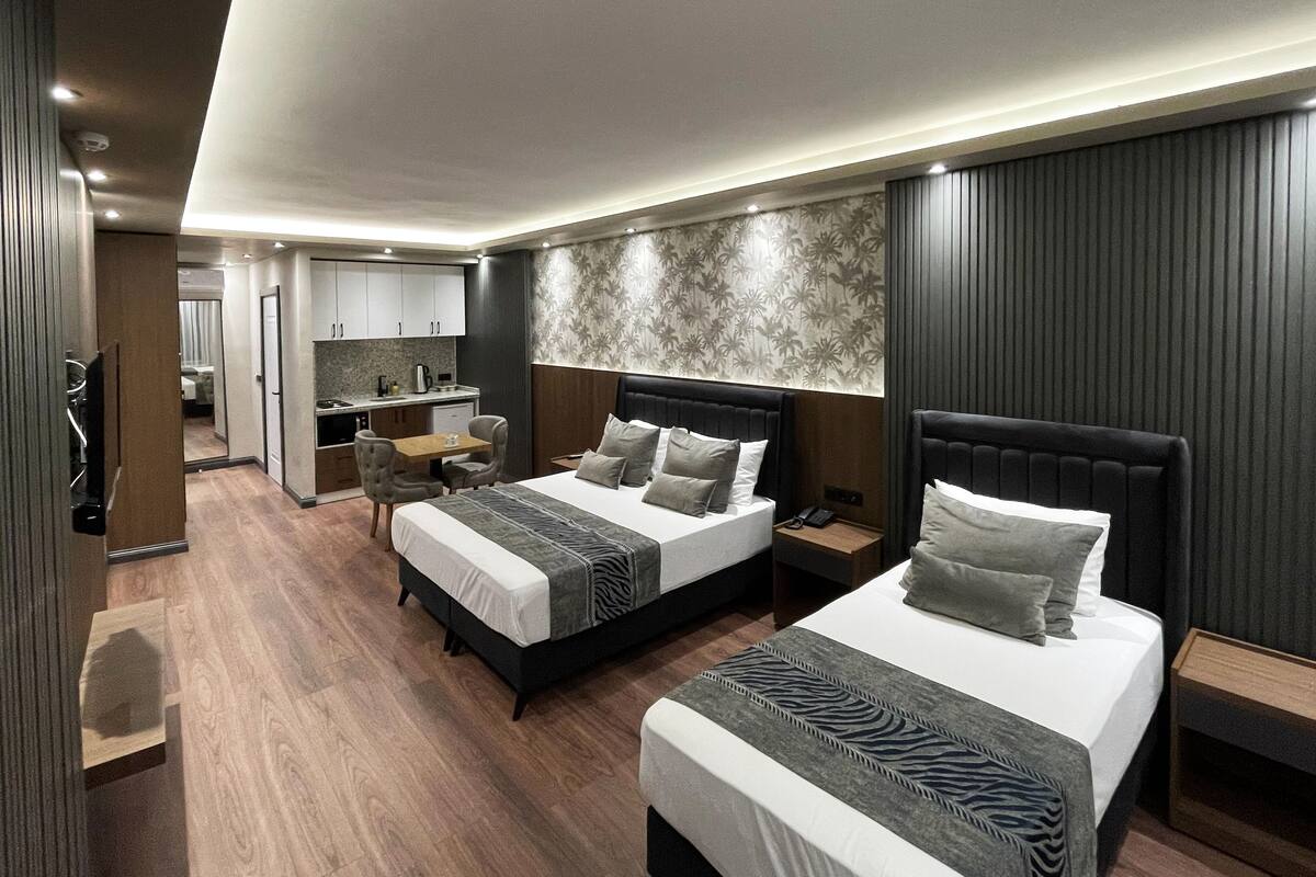 A modern hotel room with two beds, a small kitchenette, and a sitting area.