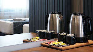 Una habitación de hotel moderna con una mesa de madera, dos hervidores eléctricos, una cafetera y una bandeja con bolsitas de té y un sobre de azúcar.
