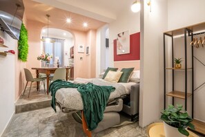 Une chambre à coucher de taille modeste, comprenant un lit, un bureau et une chaise. On y trouve une petite plante et une étagère où sont rangées des chaussures.