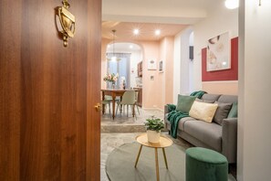 Un salon moderne avec un canapé gris, une petite table ronde agrémentée d’une plante et un pouf vert. On aperçoit à l’arrière-plan un coin repas avec une table et des chaises.