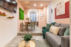 Un salon moderne avec un canapé gris, un coin repas comprenant une table et des chaises, et un téléviseur fixé au mur.