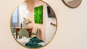Une chambre à coucher avec un lit, une couverture verte, une chaise verte, une table en bois ornée d’un vase de fleurs et un miroir fixé au mur.