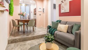Un salon moderne avec un canapé gris, une table à manger avec des chaises, et une cuisine en arrière-plan.