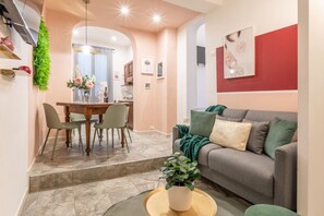Un salon moderne avec un canapé gris, une table à manger avec des chaises, et une cuisine en arrière-plan.