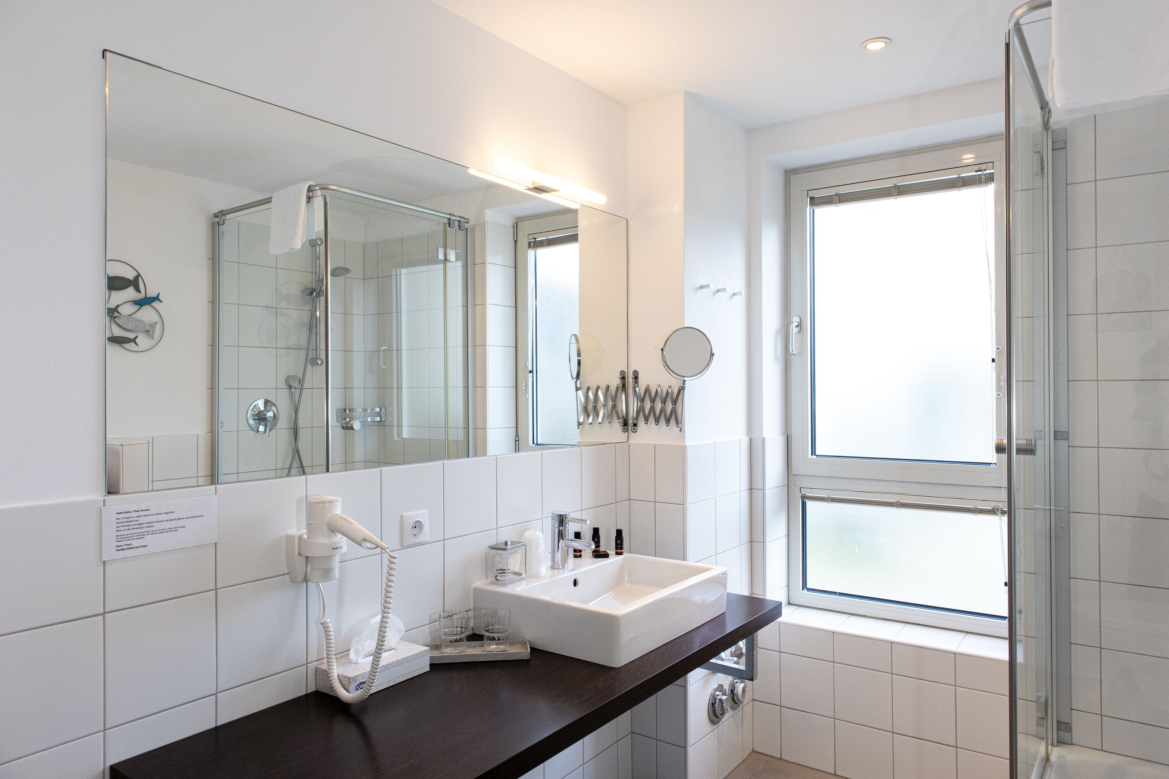 Un baño moderno con cabina de ducha de vidrio, un espejo grande y un lavabo blanco sobre encimera oscura.