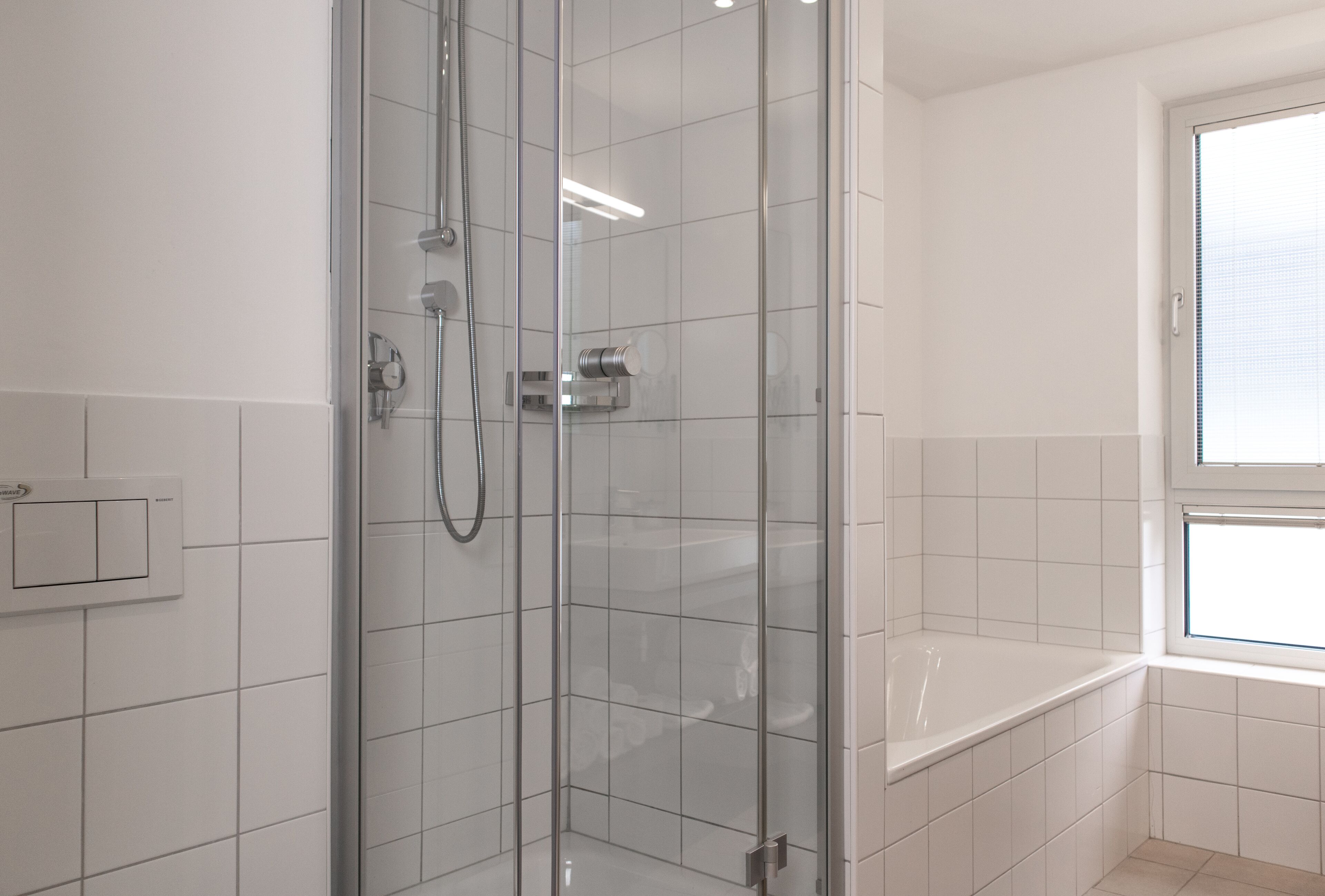 Une salle de bain moderne avec une douche à parois de verre, une baignoire blanche et une fenêtre laissant entrer la lumière naturelle.