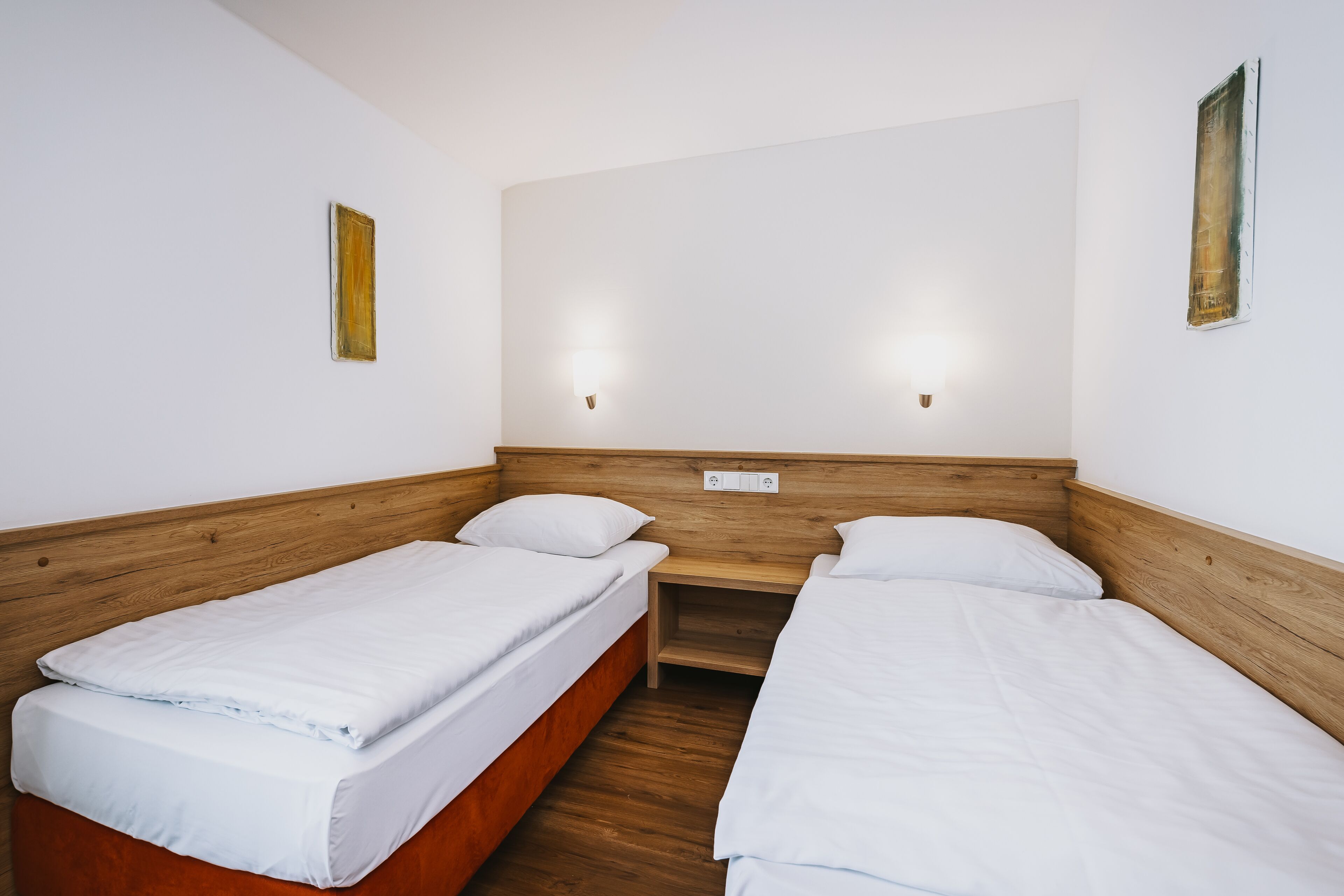 A twin room with two single beds, wooden headboard, white bedding, and two wall-mounted lights.