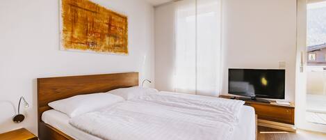 A modern bedroom with a wooden bed, a flat-screen TV, and a large window.