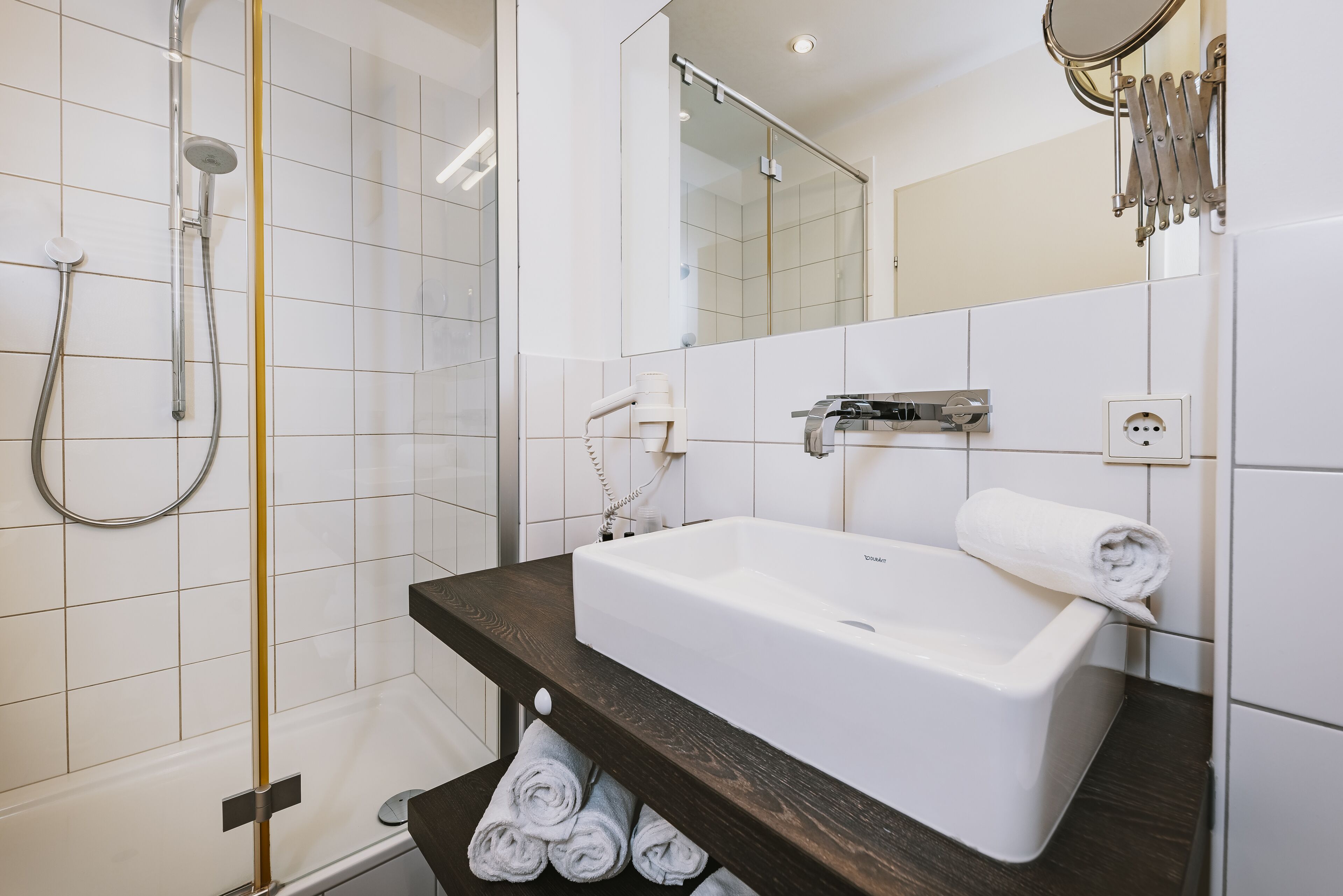 A modern bathroom with a white bathtub, a shower with a glass door, and a wooden vanity.