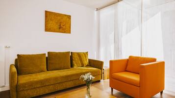 A living room with a mustard sofa, an orange armchair, and a vase with flowers on a wooden coffee table.