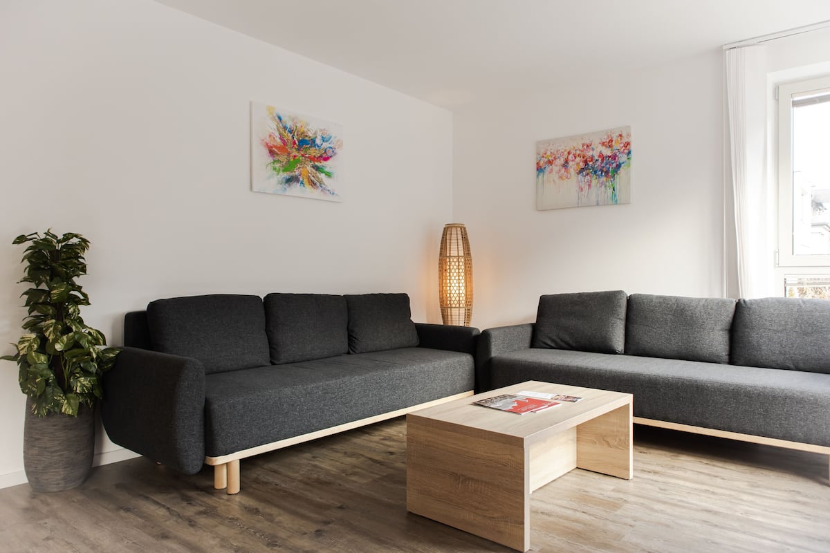 A modern living room with a grey sectional sofa, a wooden coffee table, and two abstract paintings on the walls.