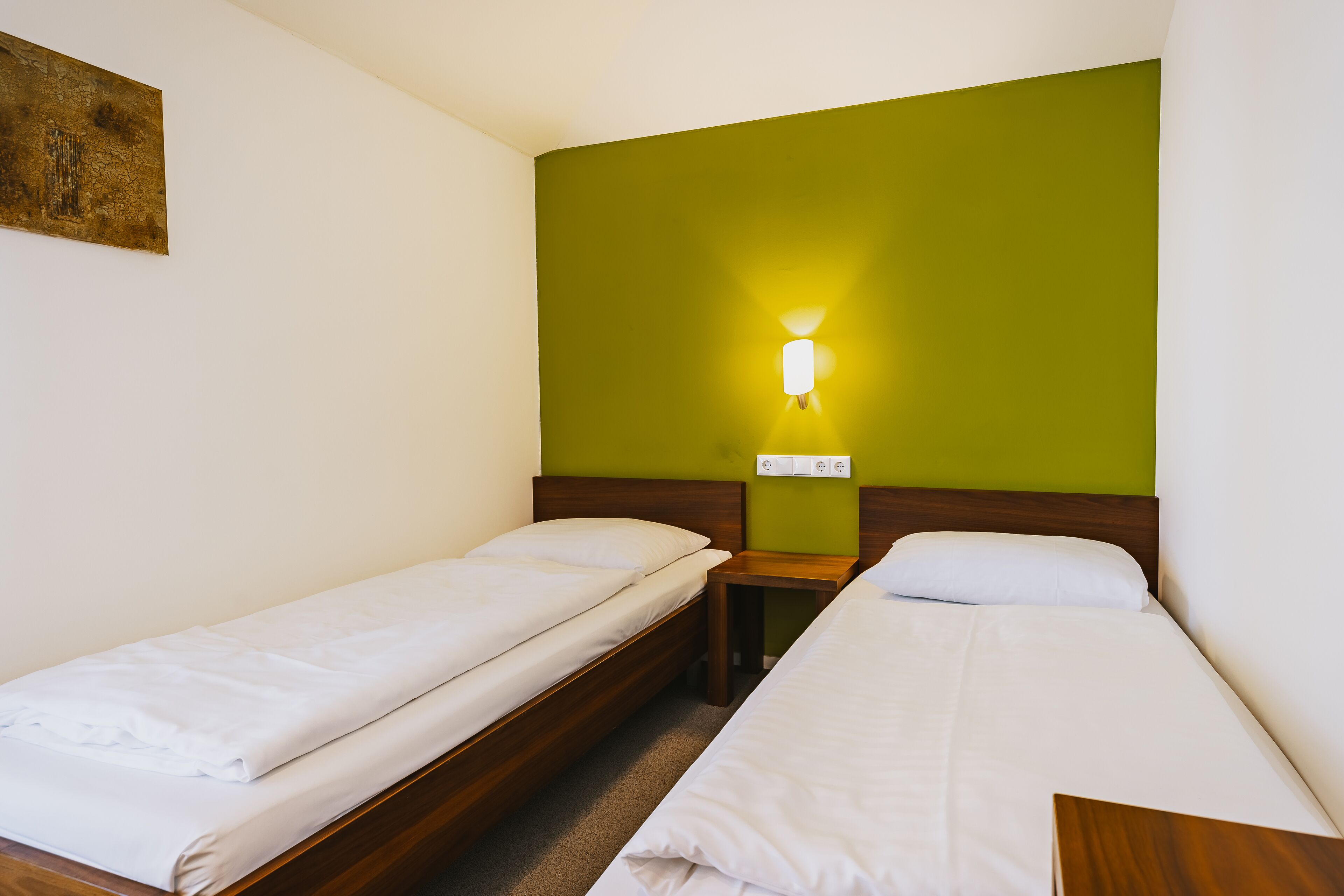 Ein Hotelzimmer mit zwei Einzelbetten, einem Nachttisch, einer Wandlampe und einer grünen Akzentwand.