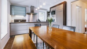 A modern kitchen with a wooden dining table, built-in appliances, and a large window. - Der Gletscherblick by Alpin Rentals - incl Summercard  (Kaprun)