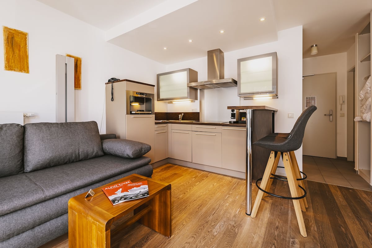 A modern living room with a grey sofa, wooden coffee table, and a bar stool.