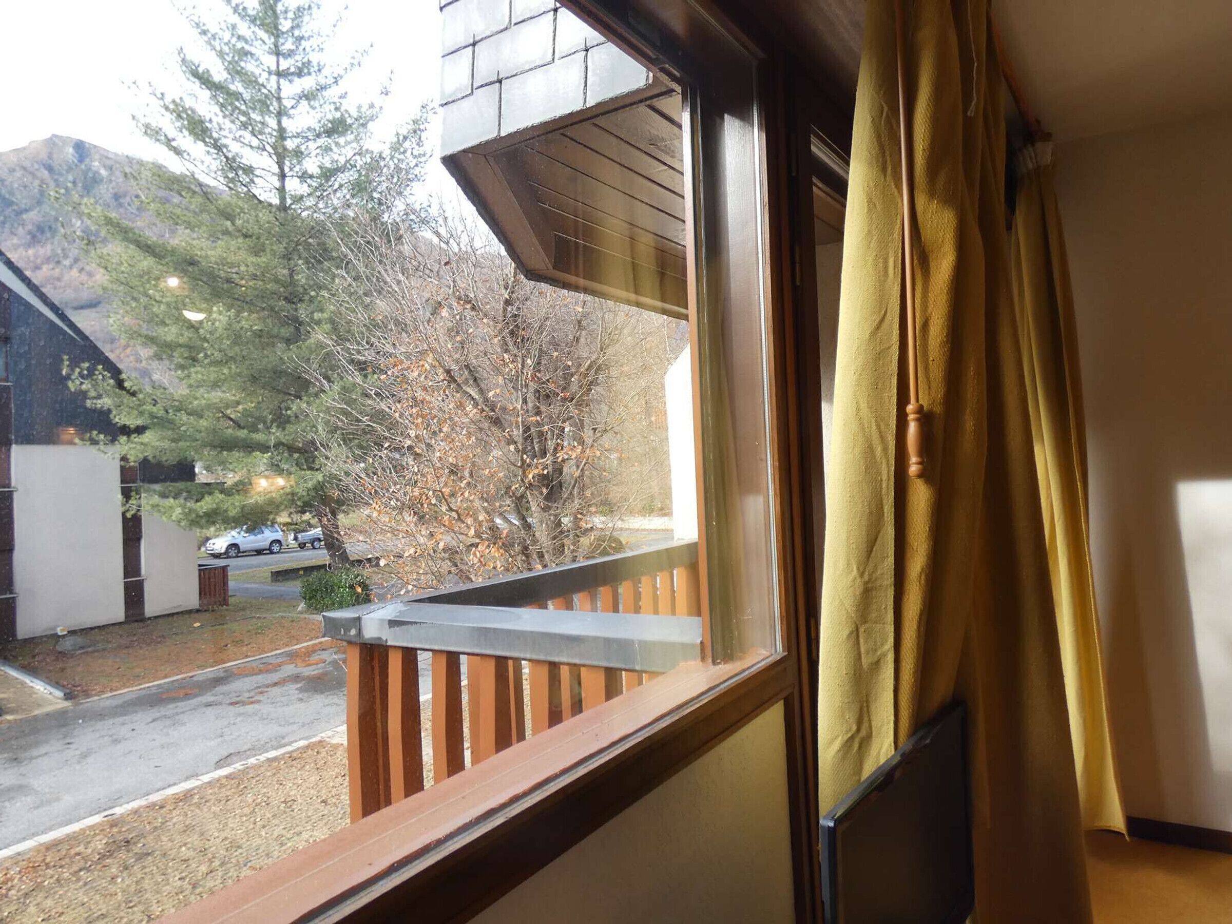 A balcony with a wooden railing and a window with yellow curtains.