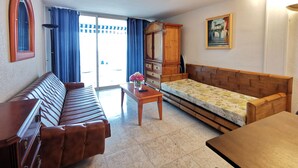 Una sala de estar con un sofá, un aparador de madera, una mesita con un jarrón y un cuadro en la pared.
