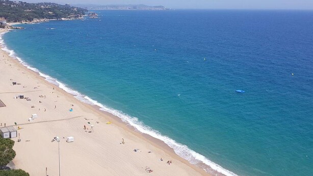 Una playa con vista despejada al océano, una orilla arenosa y edificios a lo lejos.