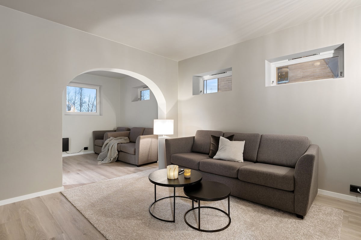 A modern living room with a grey sofa, two armchairs, a coffee table, and a fireplace.
