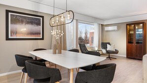 A modern dining area with a white table and dark chairs, a large framed picture on the wall, and a hanging light fixture. - The View (Tromsø)