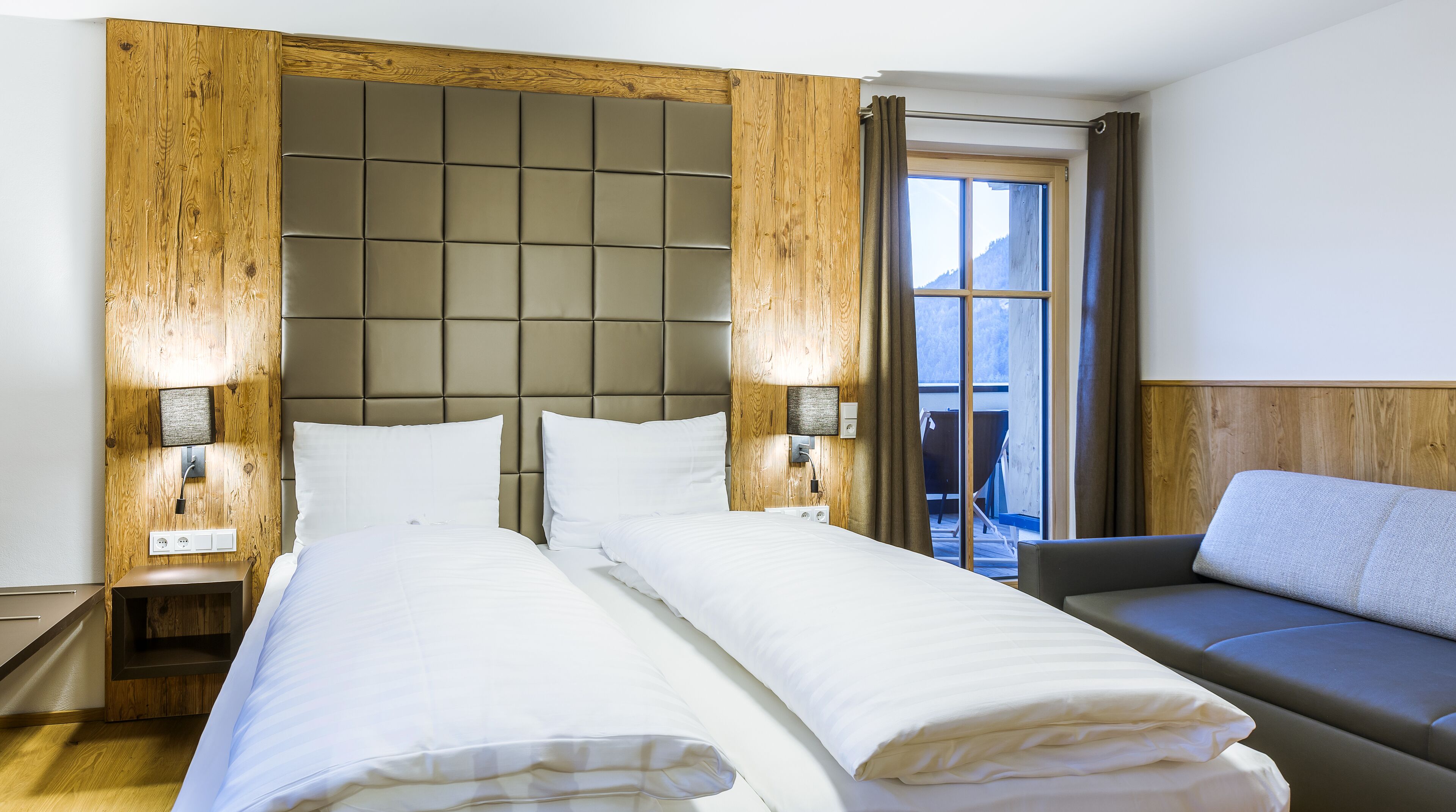 Ein Hotelzimmer mit einem großen Bett, einer Sitzecke, Holzvertäfelung und Blick ins Freie.