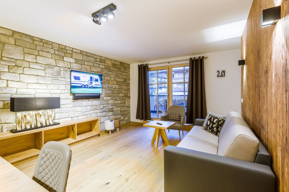 A living room with a stone wall, a television, a wooden table, and a sofa.