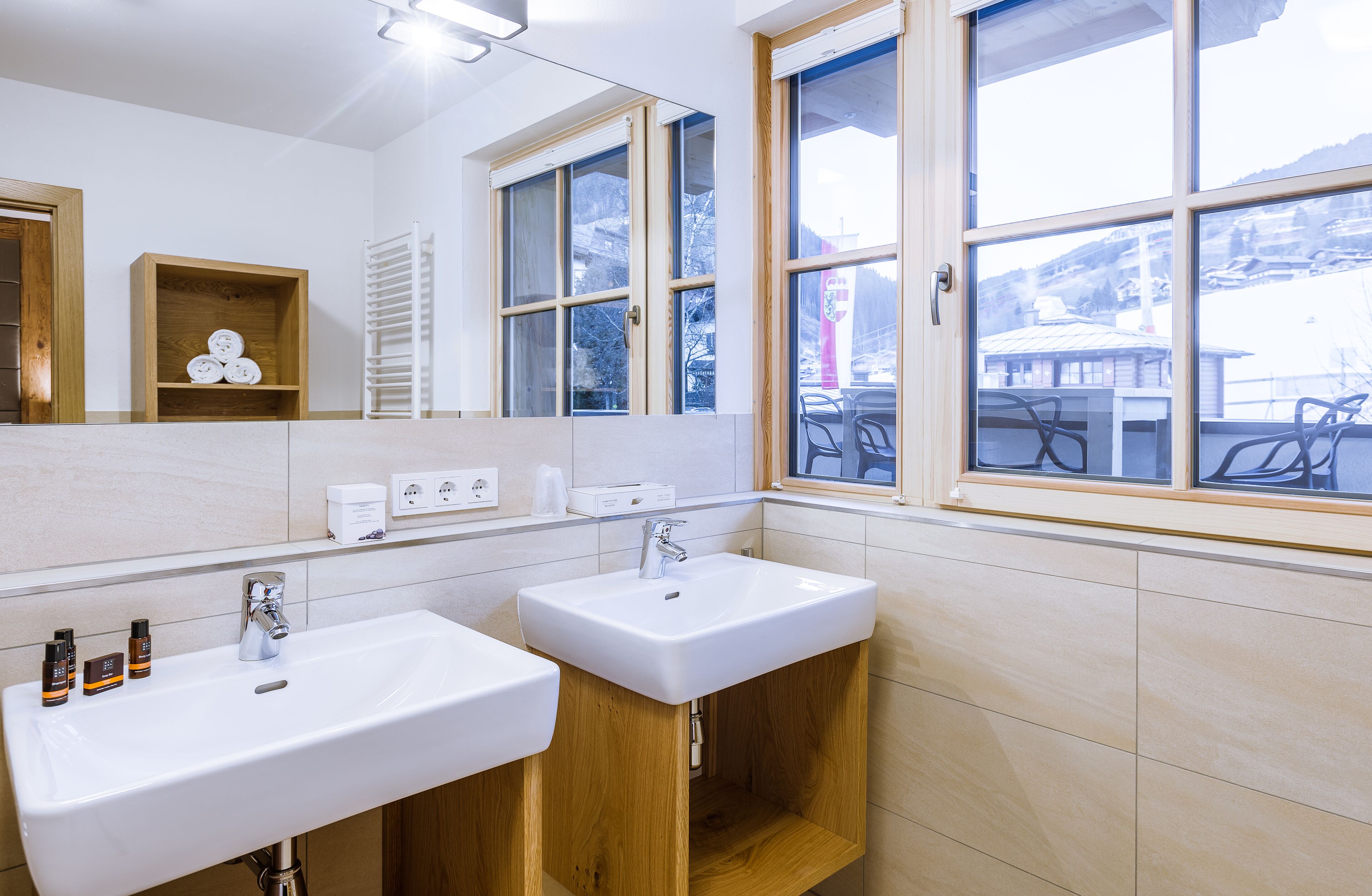 A bathroom with two sinks, a mirror, and a window with a view of a building and trees.