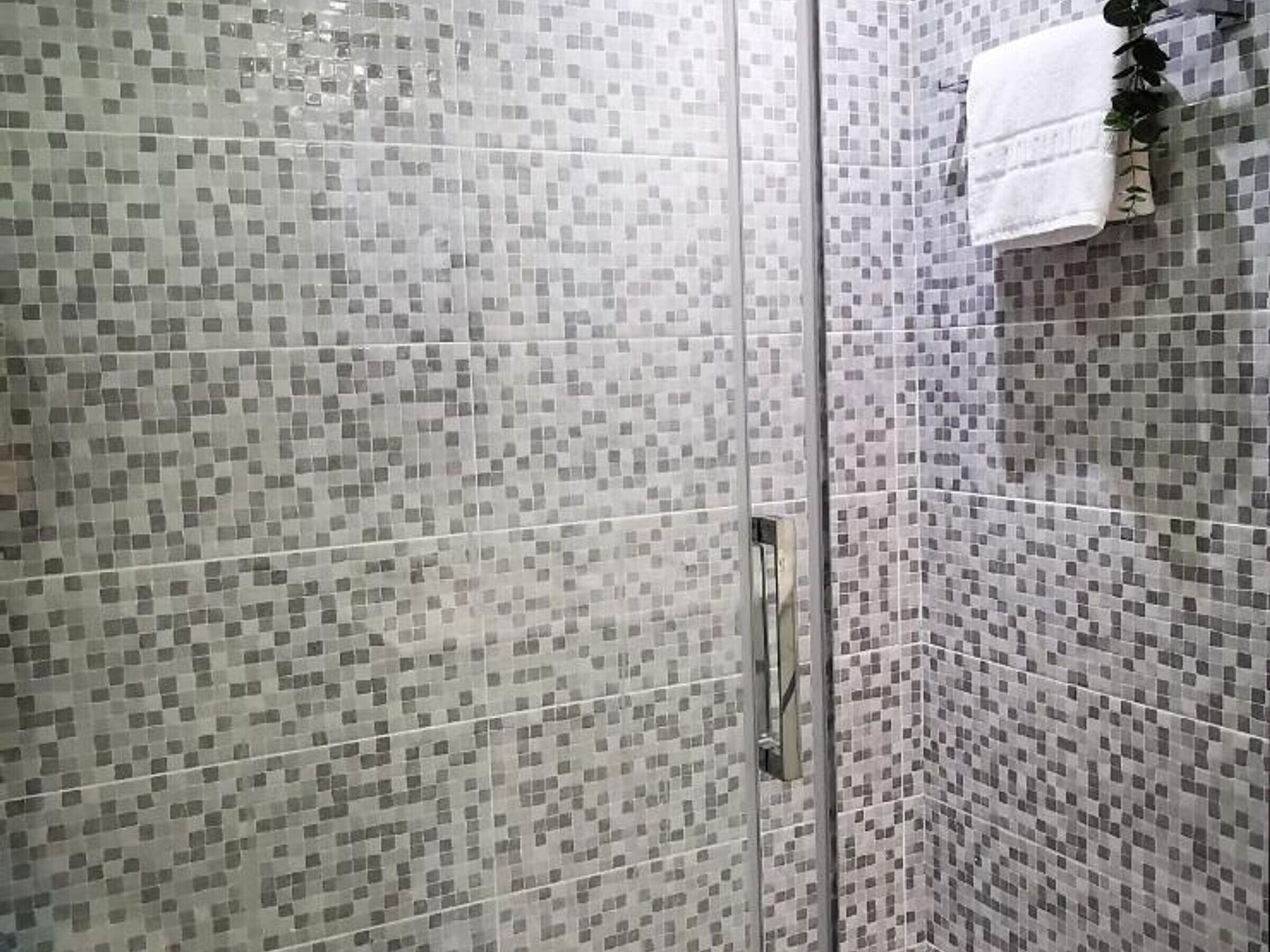 A shower area with mosaic tile walls and a glass door.