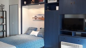 Un dormitorio con cama, televisor y estante empotrado con objetos decorativos.