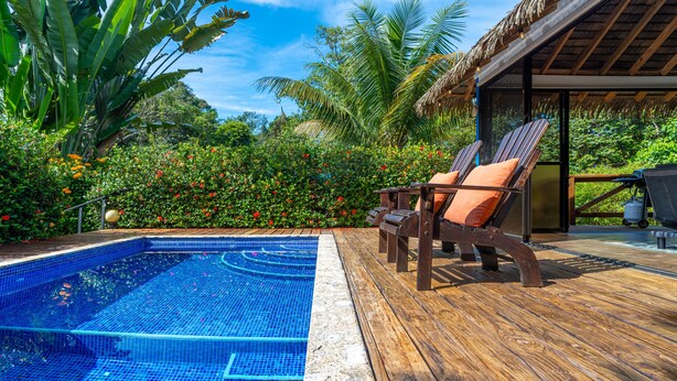 A wooden deck with two lounge chairs, a swimming pool, and lush tropical vegetation. - Cute. Cozy. Private. Pool. Ojochal. (Ojochal)