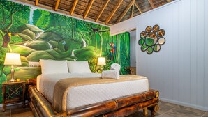 A bedroom with a large bed, wooden headboard, and a mural of a forest scene. There are two bedside tables with lamps. - Cute. Cozy. Private. Pool. Ojochal. (Ojochal)