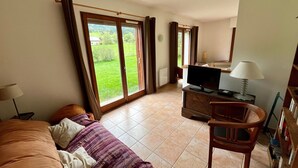 A room with a bed, a TV, a desk, and a chair. There are large windows with curtains, and a view of greenery outside. - Spacious house for 8, 4 bedrooms, mountain view (Corrençon-en-Vercors)