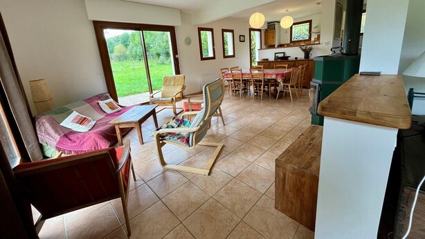 A spacious living area with a dining table and chairs, a kitchen area with a stove, and large windows offering a view of the outdoors. - Spacious house for 8, 4 bedrooms, mountain view (Corrençon-en-Vercors)