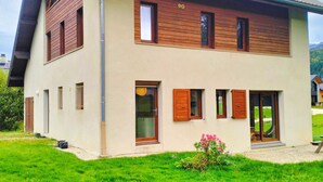 A two-story house with a sloped roof, wooden window shutters, and a small garden with pink flowers. - Spacious house for 8, 4 bedrooms, mountain view (Corrençon-en-Vercors)