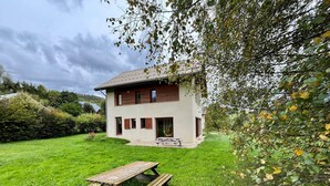 A two-story house with a wooden deck and a picnic table in the front yard. - Spacious house for 8, 4 bedrooms, mountain view (Corrençon-en-Vercors)