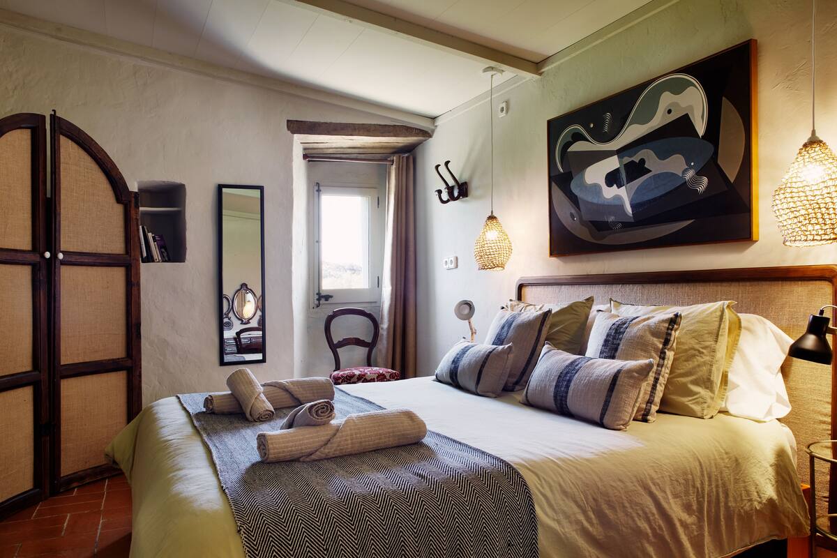 Quarto bem iluminado com uma cama grande, um guarda-roupa de madeira, um espelho e um quadro na parede.