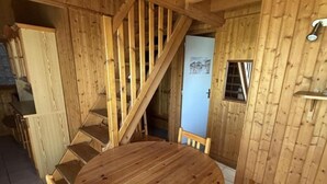 Una mesa de comedor de madera con sillas, una escalera y una puerta con ventanal.