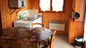 Cocina compacta con paredes de madera, una mesa con mantel floral, un lavamanos, un microondas y un refrigerador.
