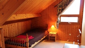 Una habitación pequeña y acogedora con una cama de madera, una mesita de noche, una lámpara y una ventana con vistas.
