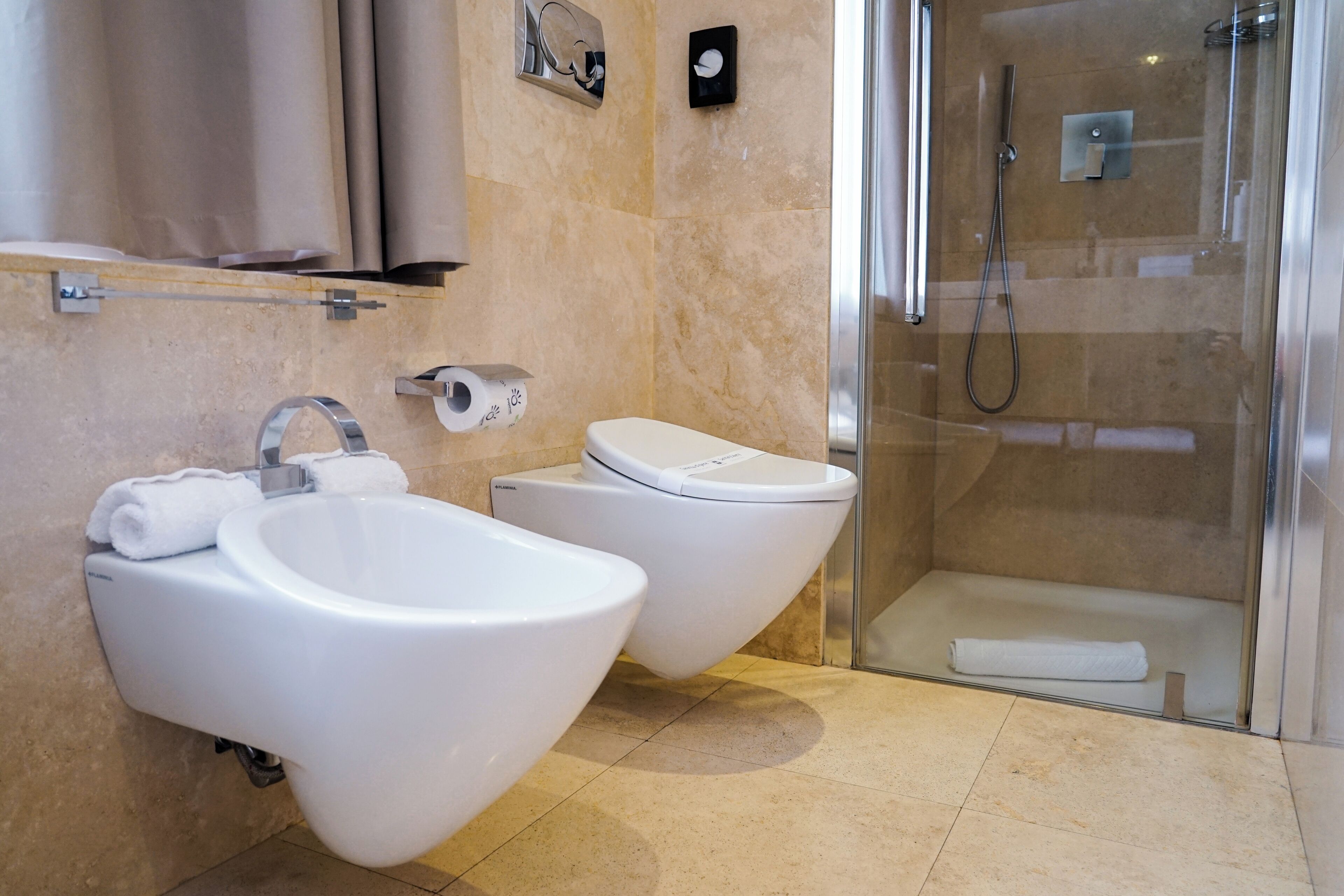 Un baño moderno con dos bidés, ducha con cerramiento de vidrio y suelo de mármol.