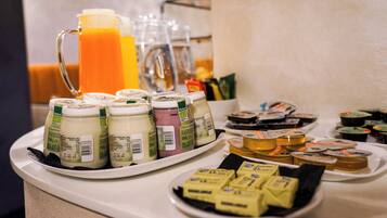 Buffet de café da manhã com diversas opções de alimentos e um jarro grande de suco de laranja.