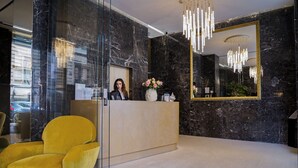 Un espace d’accueil avec un mur de marbre, un comptoir de réception, un fauteuil jaune et un grand miroir.