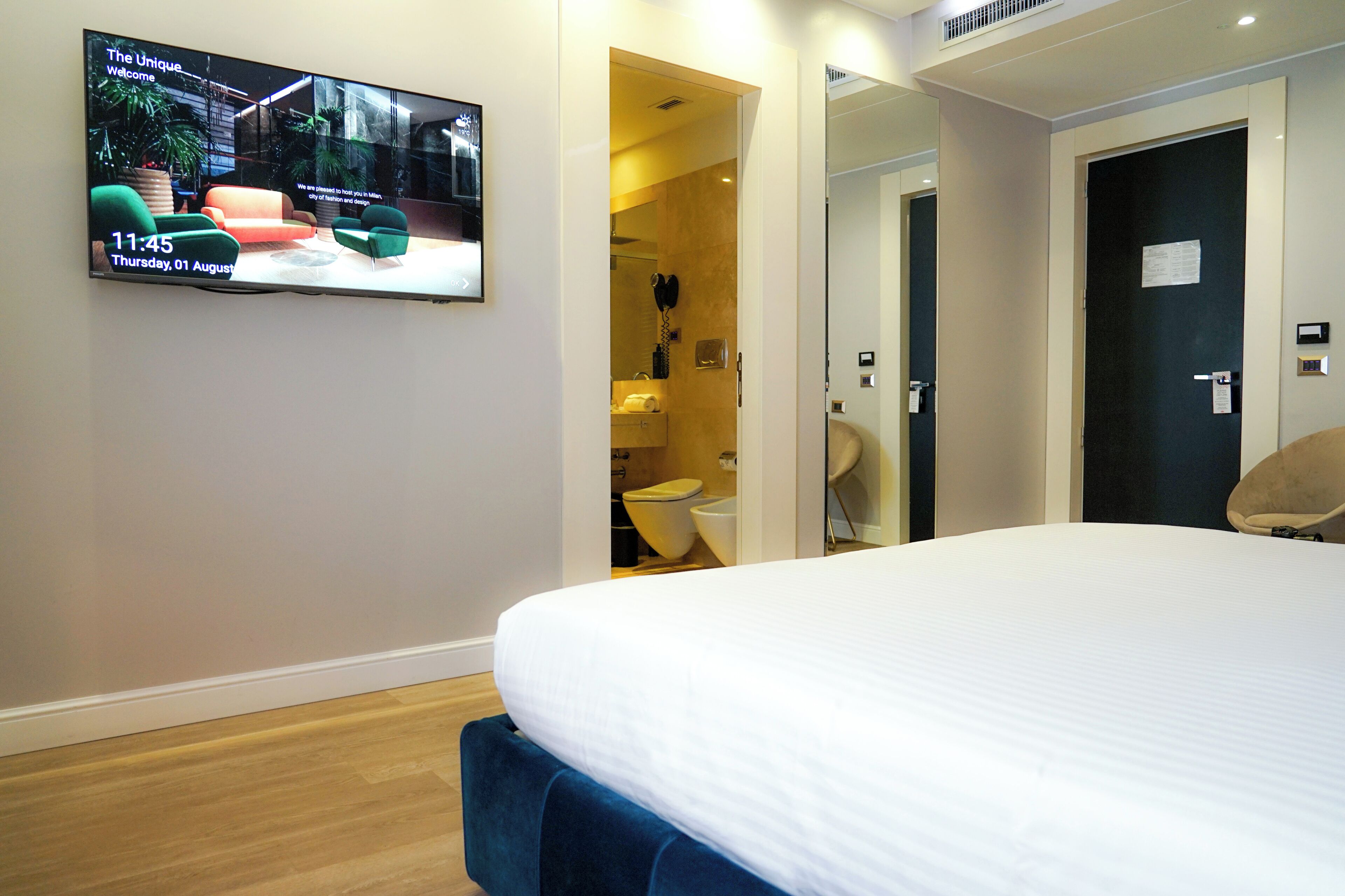 A hotel room with a bed, a TV mounted on the wall, and a bathroom visible through an open door.