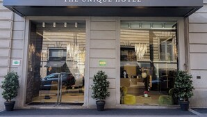 L’entrée de l’hôtel The Unique, avec sa façade en verre, ses plantes en pot et une enseigne indiquant qu’il s’agit d’un hôtel.