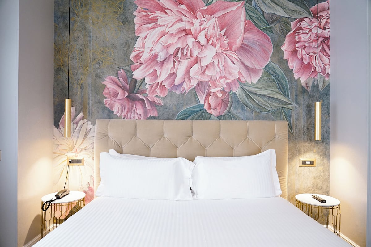 A bedroom with a large bed, a headboard, two bedside tables, and a floral mural on the wall.