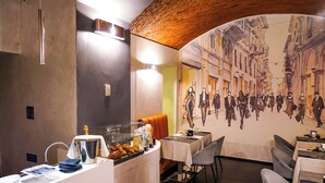 Un restaurant orné d’une fresque représentant une scène de rue historique, un buffet proposant divers plats et un coin salon confortable avec des tables et des chaises.