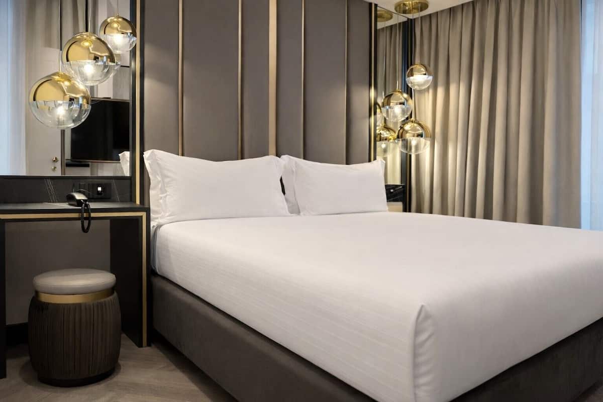 A modern hotel room with a large bed, a desk, and a vanity.