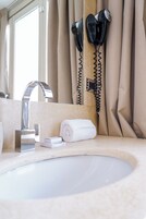 A bathroom with a white sink, a mirror, a towel, and a hairdryer mounted on the wall.