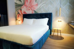 Una cama bien tendida con un cabecero azul, una pared con un gran mural floral y dos luces fijadas a la pared.