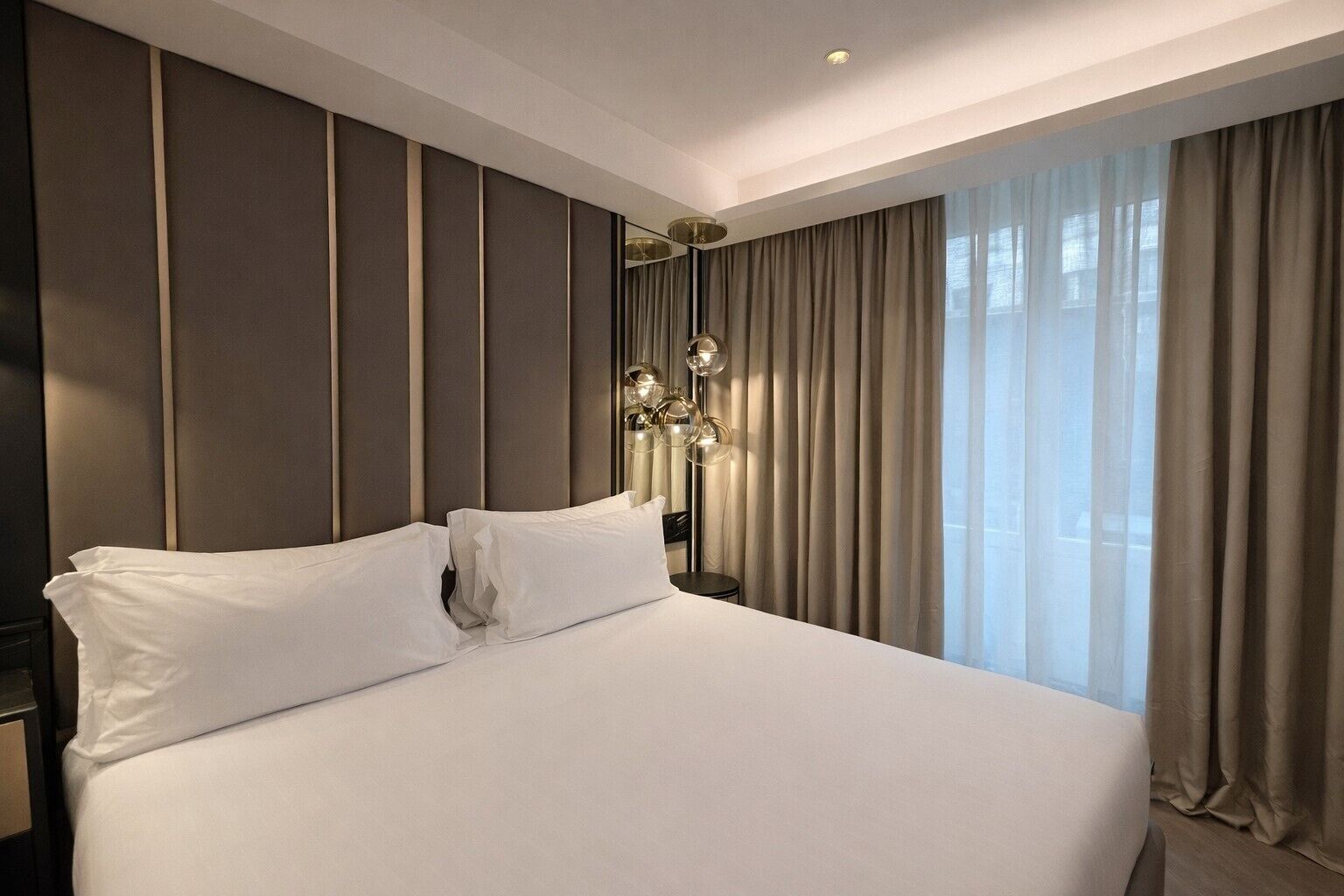 A hotel room with a large bed, a bedside lamp, and a view of the outdoors through the window.