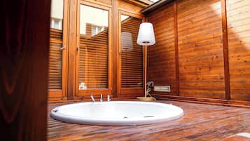 A wooden interior with a round bathtub, a white lamp, and a window with blinds.